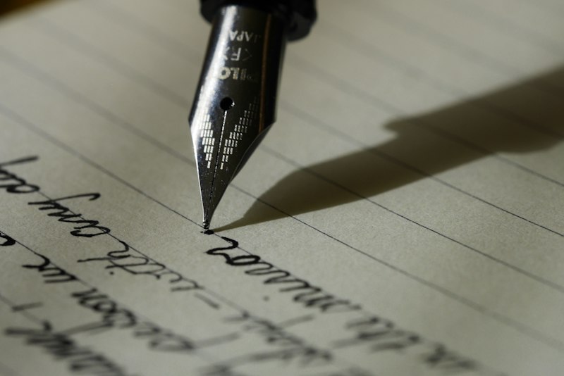 A person writing notes in a paper notebook with a pen