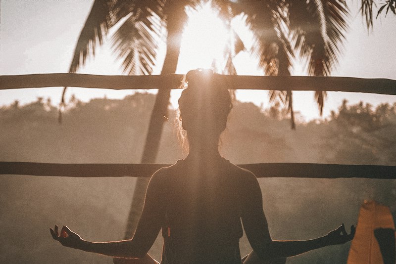 A person standing outdoors at sunset with arms raised, taking a break